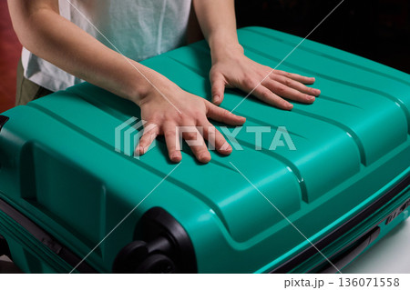 Traveler opening luggage, Close shot of hands unfastening suitcase zipper before travel, Detailed view of hands pulling zipper on vibrant teal travel case with anticipation Traveler opening luggage, Close shot of hands unfastening suitcase zipper before travel, Detailed view of hands pulling zipper on vibrant teal travel case with anticipation 136071558