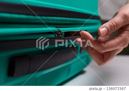 Traveler opening luggage, Close shot of hands unfastening suitcase zipper before travel, Detailed view of hands pulling zipper on vibrant teal travel case with anticipation 136071567