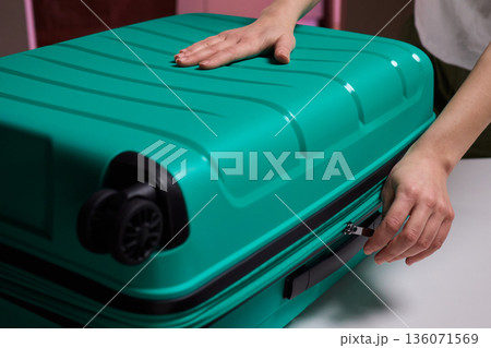 Traveler opening luggage, Close shot of hands unfastening suitcase zipper before travel, Detailed view of hands pulling zipper on vibrant teal travel case with anticipation Traveler opening luggage, Close shot of hands unfastening suitcase zipper before travel, Detailed view of hands pulling zipper on vibrant teal travel case with anticipation 136071569