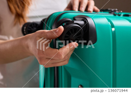 Inspecting suitcase wheels for strength and smooth operation before travel, Traveler thoroughly assesses condition and reliability of suitcase wheels for upcoming journey 136071944