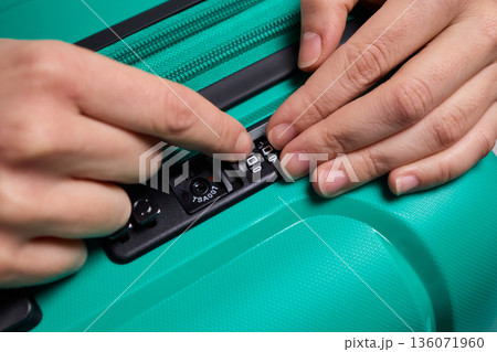 Secure suitcase with combo lock, Hands set combination on teal suitcase with textured surface, Closeup of hands adjusting numeric lock on stylish teal travel suitcase Secure suitcase with combo lock, Hands set combination on teal suitcase with textured surface, Closeup of hands adjusting numeric lock on stylish teal travel suitcase 136071960