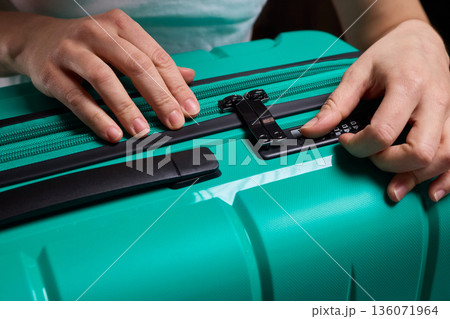 Secure suitcase with combo lock, Hands set combination on teal suitcase with textured surface, Closeup of hands adjusting numeric lock on stylish teal travel suitcase Secure suitcase with combo lock, Hands set combination on teal suitcase with textured surface, Closeup of hands adjusting numeric lock on stylish teal travel suitcase 136071964