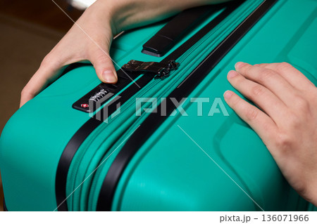 Secure suitcase with combo lock, Hands set combination on teal suitcase with textured surface, Closeup of hands adjusting numeric lock on stylish teal travel suitcase Secure suitcase with combo lock, Hands set combination on teal suitcase with textured surface, Closeup of hands adjusting numeric lock on stylish teal travel suitcase 136071966