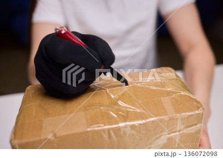 Worker examines package cautiously, Warehouse employee checks sealed box meticulously, Focused employee carefully inspects and cuts tape on parcel in warehouse setting Worker examines package cautiously, Warehouse employee checks sealed box meticulously, Focused employee carefully inspects and cuts tape on parcel in warehouse setting 136072098