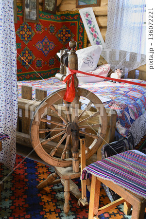 A fragment of the interior of a 19th-century rustic hut with a wooden spinning wheel and a bed 136072221