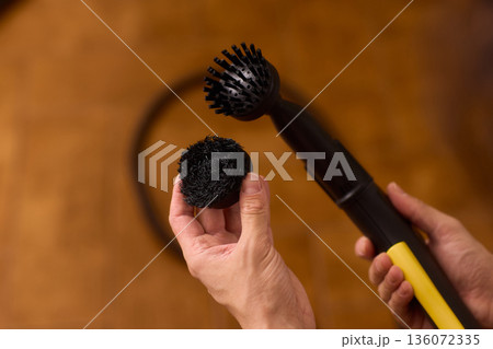 Household brushes examined closely, Two brushes analyzed in indoor setting, Person holding two black brushes inspecting bristle arrangement for household cleaning purposes 136072335