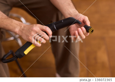 Steam cleaning device being prepared for upholstery and grout cleaning tasks. Focus on textured grip and soft plastic with warm background indicating household maintenance 136072365