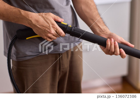 Steam cleaning device being prepared for upholstery and grout cleaning tasks. Focus on textured grip and soft plastic with warm background indicating household maintenance Steam cleaning device being prepared for upholstery and grout cleaning tasks. Focus on textured grip and soft plastic with warm background indicating household maintenance 136072386