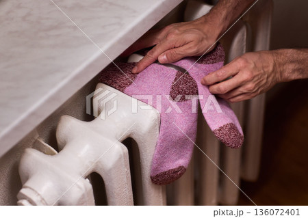 Person placing moist wool socks onto heated radiator fins, Detailed scene of hand carefully positioning damp wool socks on heated metal radiator with knit texture 136072401