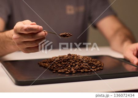 Detail oriented scene of coffee professional measuring beans carefully, An intimate scene depicting barista accurately measuring roasted coffee beans with gold scoop 136072434