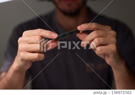 Individual carefully inspecting SODIMM memory module in detailed review, Technician performing detailed visual assessment of RAM stick with neutral lighting and focused attention 136072502