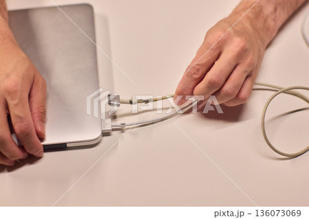 Repairing laptop power cord, Detailed image of fixing broken laptop charger wire, Closeup of skillful person restoring worn electrical cord for portable computer 136073069