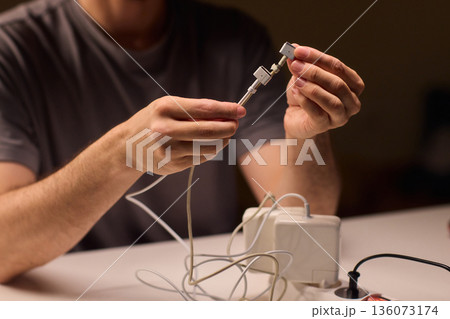 Repairing damaged cable, Hands carefully inspecting damaged laptop power cable insulation, Focused closeup of hands troubleshooting frayed wires and exposed copper connectors 136073174