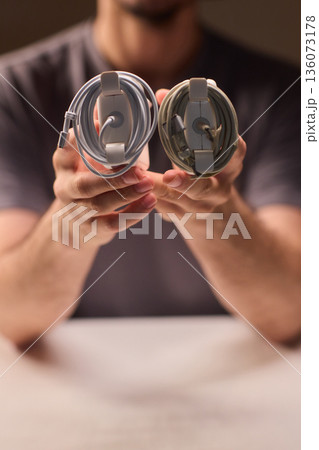 Person examines frayed charger cord, Close view of broken laptop power cable, Manual inspection of worn out electronic cable emphasizing repair and safety concerns 136073178