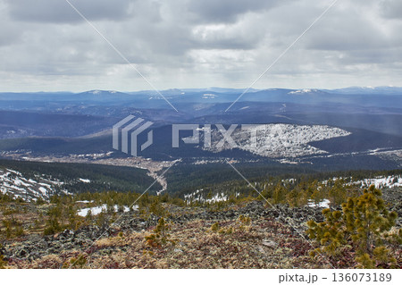 Panorama of a mountain range with patches of snow and dark forest on a cloudy day. Scenic natural landscape for travel and adventure. Panorama of a mountain range with patches of snow and dark forest on a cloudy day. Scenic natural landscape for travel and adventure. 136073189