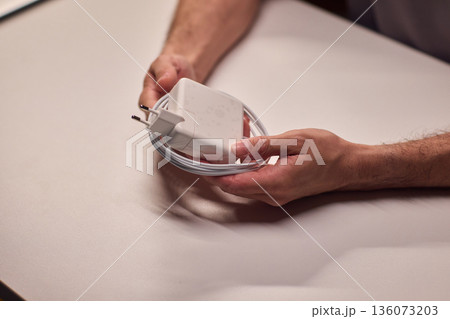 Technician examining charger carefully, Closeup of hands inspecting laptop cable, Meticulous technician performing detailed inspection of laptop power supply before packaging Technician examining charger carefully, Closeup of hands inspecting laptop cable, Meticulous technician performing detailed inspection of laptop power supply before packaging 136073203