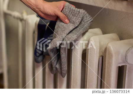 Person placing moist wool socks onto heated radiator fins, Detailed scene of hand carefully positioning damp wool socks on heated metal radiator with knit texture Person placing moist wool socks onto heated radiator fins, Detailed scene of hand carefully positioning damp wool socks on heated metal radiator with knit texture 136073314