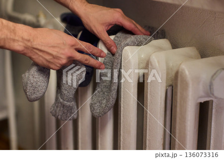 Person placing moist wool socks onto heated radiator fins, Detailed scene of hand carefully positioning damp wool socks on heated metal radiator with knit texture 136073316