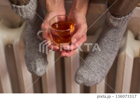 Person with knit socks warming by radiator, Cozy winter scene with steaming mug and drying socks, Tranquil winter morning with warm amber glow and relaxing foot warmers 136073317