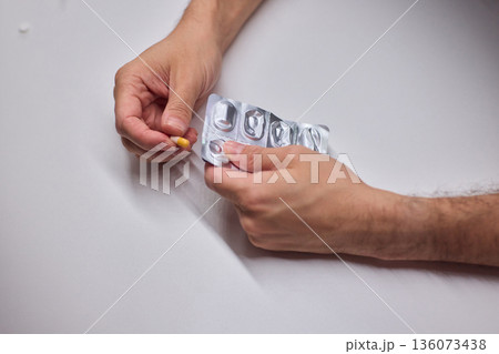Hands extracting capsule from blister pack gently, closeup on fingertips and foil on white tabletop, quiet moment of dosing accuracy and calm preparation for intake 136073438