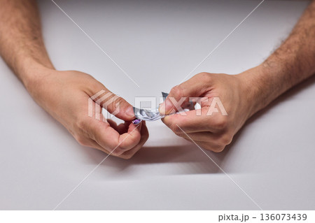 Hands extracting capsule from blister pack gently, closeup on fingertips and foil on white tabletop, quiet moment of dosing accuracy and calm preparation for intake 136073439