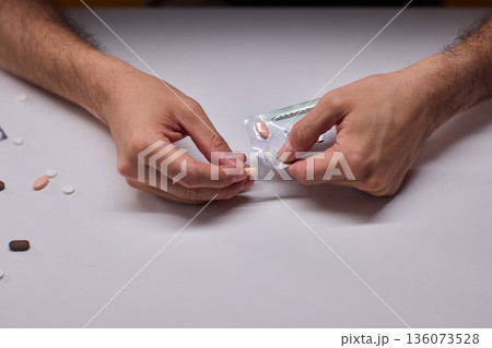 Hands extracting capsule from blister pack gently, closeup on fingertips and foil on white tabletop, quiet moment of dosing accuracy and calm preparation for intake 136073528