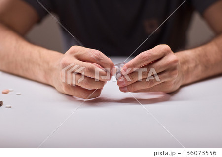 Hands extracting capsule from blister pack gently, closeup on fingertips and foil on white tabletop, quiet moment of dosing accuracy and calm preparation for intake 136073556