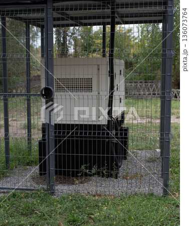 Installation of a large industrial fuel-fired generator on a green lawn. A mobile power source, backup equipment for power plants. Installation of a large industrial fuel-fired generator on a green lawn. A mobile power source, backup equipment for power plants. 136073764
