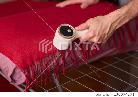 Hands cleaning red wool scarf with lint roller across fringed fabric, closeup texture, warm bedroom lighting, careful motion, pet hair removal, garment ready for outing 136074271