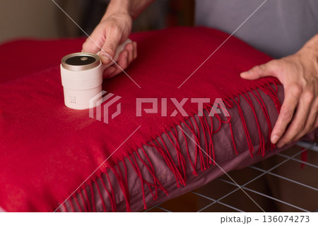 Hands cleaning red wool scarf with lint roller across fringed fabric, closeup texture, warm bedroom lighting, careful motion, pet hair removal, garment ready for outing Hands cleaning red wool scarf with lint roller across fringed fabric, closeup texture, warm bedroom lighting, careful motion, pet hair removal, garment ready for outing 136074273