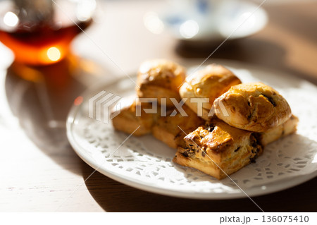 窓からの自然光に照らされる白い皿のスコーンとティーセット 窓からの自然光に照らされる白い皿のスコーンとティーセット 136075410