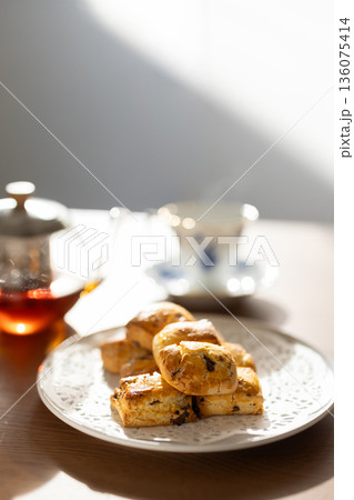 窓からの自然光に照らされる白い皿のスコーンとティーセット 136075414