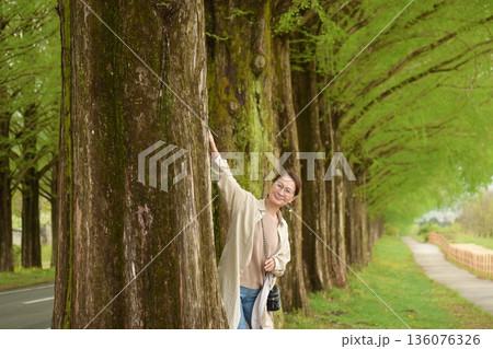 新緑のメタセコイヤ並木道を笑顔で散歩する女性 136076326