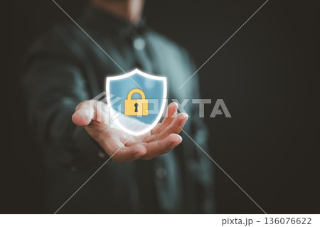 Businessman holding glowing shield with lock icon representing digital security and data protection 136076622