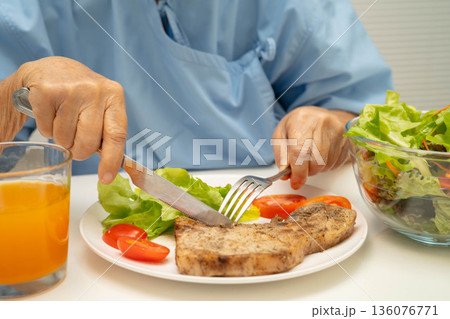 Asian elderly woman patient eating pork chop stake and vegetable salad for healthy food in hospital. Asian elderly woman patient eating pork chop stake and vegetable salad for healthy food in hospital. 136076771