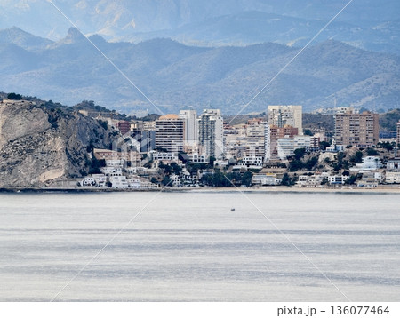 Coastal mountain scene, Distant peaks meet rugged shoreline, Hilly coast with towers and layered structures 136077464