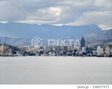 Urban horizon reflected over calm waters, City silhouette with mountain layers and tranquil bay Urban horizon reflected over calm waters, City silhouette with mountain layers and tranquil bay 136077473