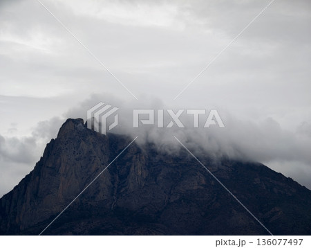 Secluded granite summit cloaked in brooding clouds amidst jagged cliffs and rugged terrain Secluded granite summit cloaked in brooding clouds amidst jagged cliffs and rugged terrain 136077497