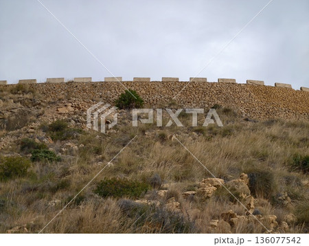 Scene displaying stone fortification atop dry hillside with sparse vegetation and rocky outcrops Scene displaying stone fortification atop dry hillside with sparse vegetation and rocky outcrops 136077542