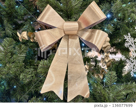 Decorative golden bow on green pine, Shimmering metallic ribbon adorns lush pine branches beautifully Decorative golden bow on green pine, Shimmering metallic ribbon adorns lush pine branches beautifully 136077699