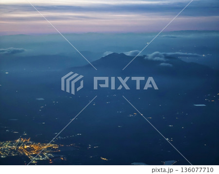 Deep blue sky showcases glowing cityscape surrounding mountain peak with volcanic profile at night 136077710