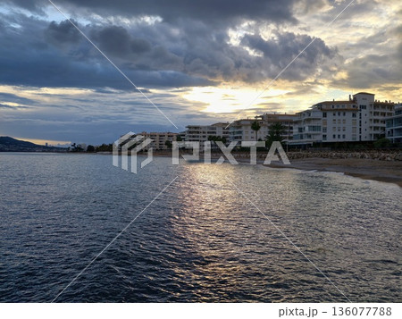 Evening waterfront showcasing sparkling water reflections and moody clouds with golden accents 136077788