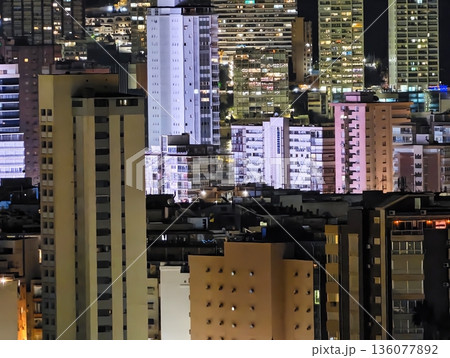 Vivid city skyline illuminated with glowing structures and energetic nighttime urban atmosphere Vivid city skyline illuminated with glowing structures and energetic nighttime urban atmosphere 136077892