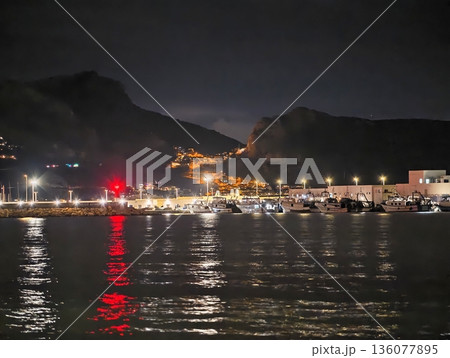Quiet waterfront illuminated by bright coastal lights reflecting off tranquil water surfaces Quiet waterfront illuminated by bright coastal lights reflecting off tranquil water surfaces 136077895