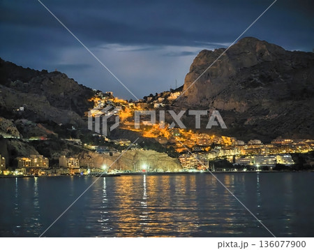 Village lights reflecting on water, Cozy hillside settlement shining across peaceful water surface at night Village lights reflecting on water, Cozy hillside settlement shining across peaceful water surface at night 136077900