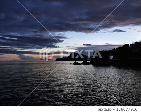 Somber skies gathering above jagged rocks while restless waters crash violently and dramatically Somber skies gathering above jagged rocks while restless waters crash violently and dramatically 136077910