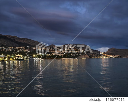Clouds reflect on water surface, Dark clouds hang above expansive coastal landscape and shimmering sea Clouds reflect on water surface, Dark clouds hang above expansive coastal landscape and shimmering sea 136077913