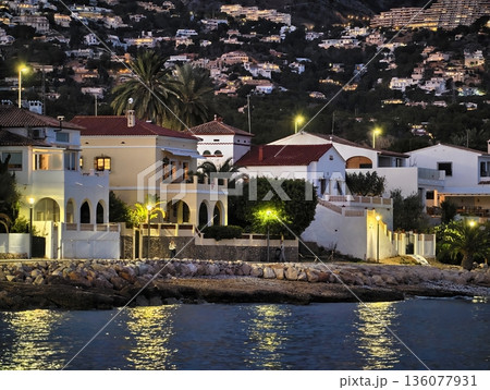 Sumptuous waterfront residences situated along peaceful rocky coast bathed in evening glow 136077931