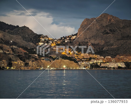 Luminous coastal village, Seaside community bordered by mountains with vibrant night illumination Luminous coastal village, Seaside community bordered by mountains with vibrant night illumination 136077933
