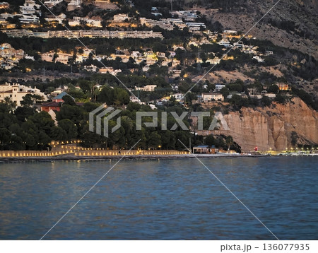 Luminous waterfront walkway, Evening leisure along tranquil shoreline with glowing lights and gentle waves 136077935